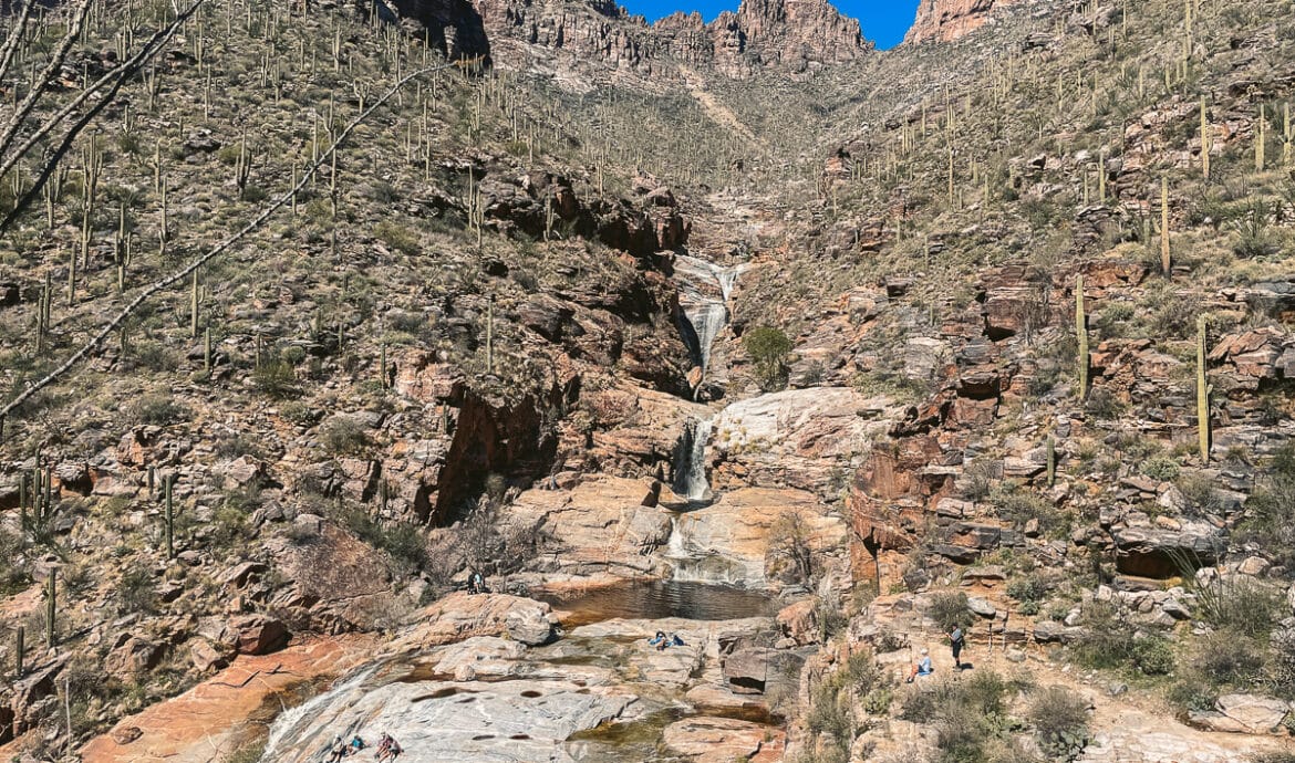 The view of Seven Falls to our left while hiking the last section. You can see a layer of waterfalls surrounded by cacti which are also surrounded by mountain peaks.