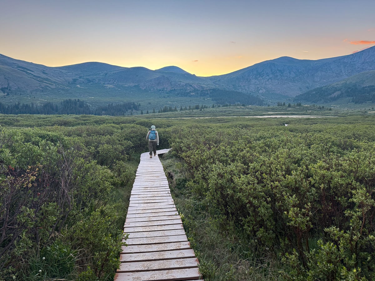 The beginning of the Mount Bierstadt trail walking along a wooden path with the sun rising above the mountains in the background. 